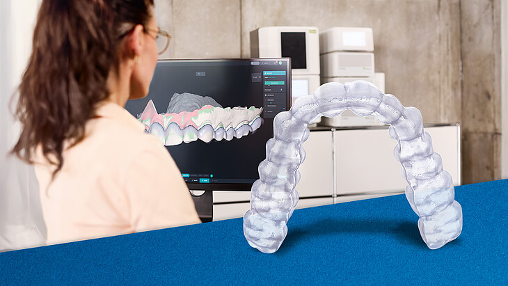 Eine Zahnärztin oder Zahntechnikerin vor einem Monitor, auf dem sie eine Aufbissschiene designt. Im Vordergrund eine fertige, 3D-gestaltete Schiene
